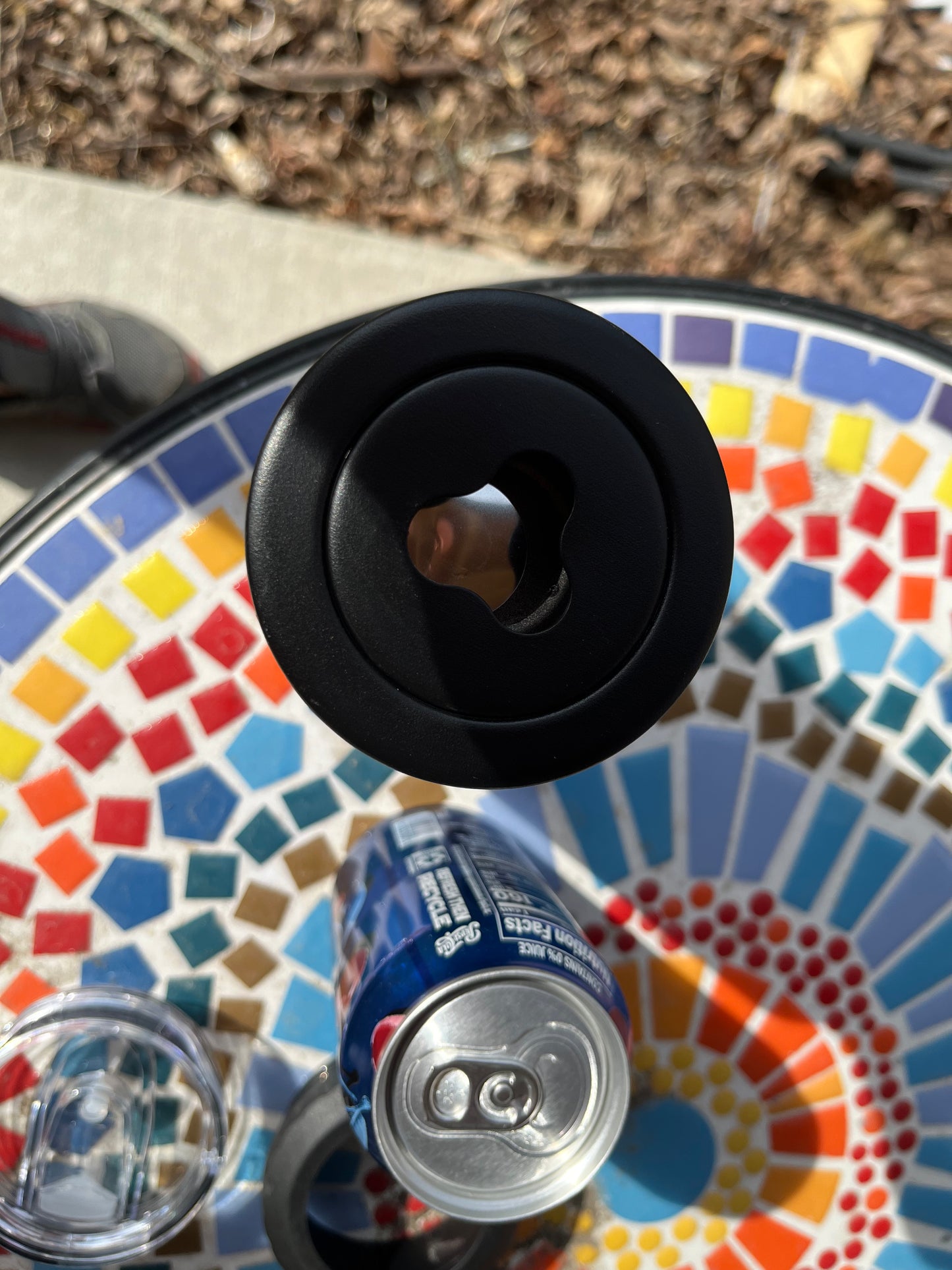 Black bottle opener on a colorful mosaic table with a can and glass.